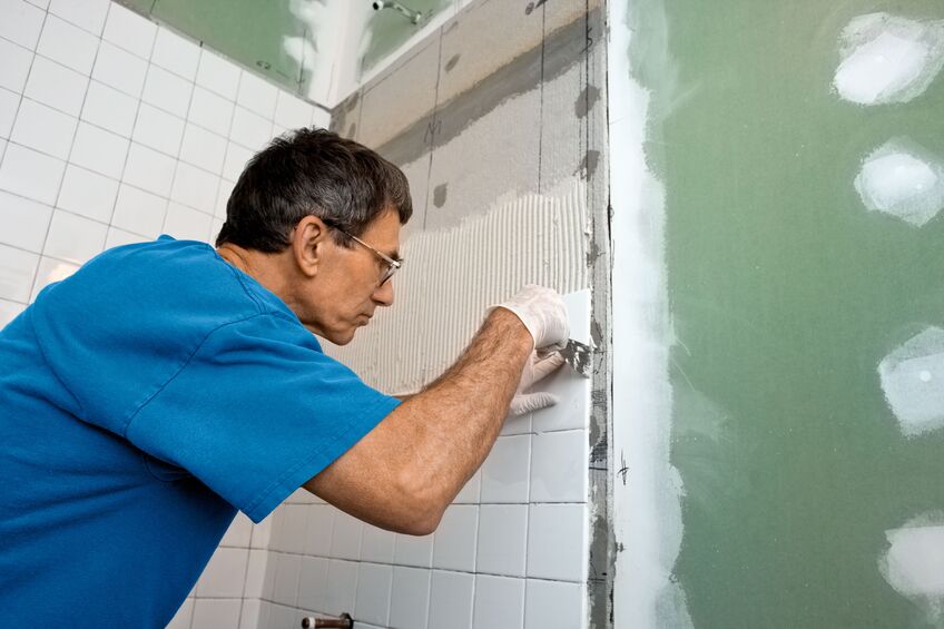 man applying ceramic tile to a bathtub enclosure wall.
